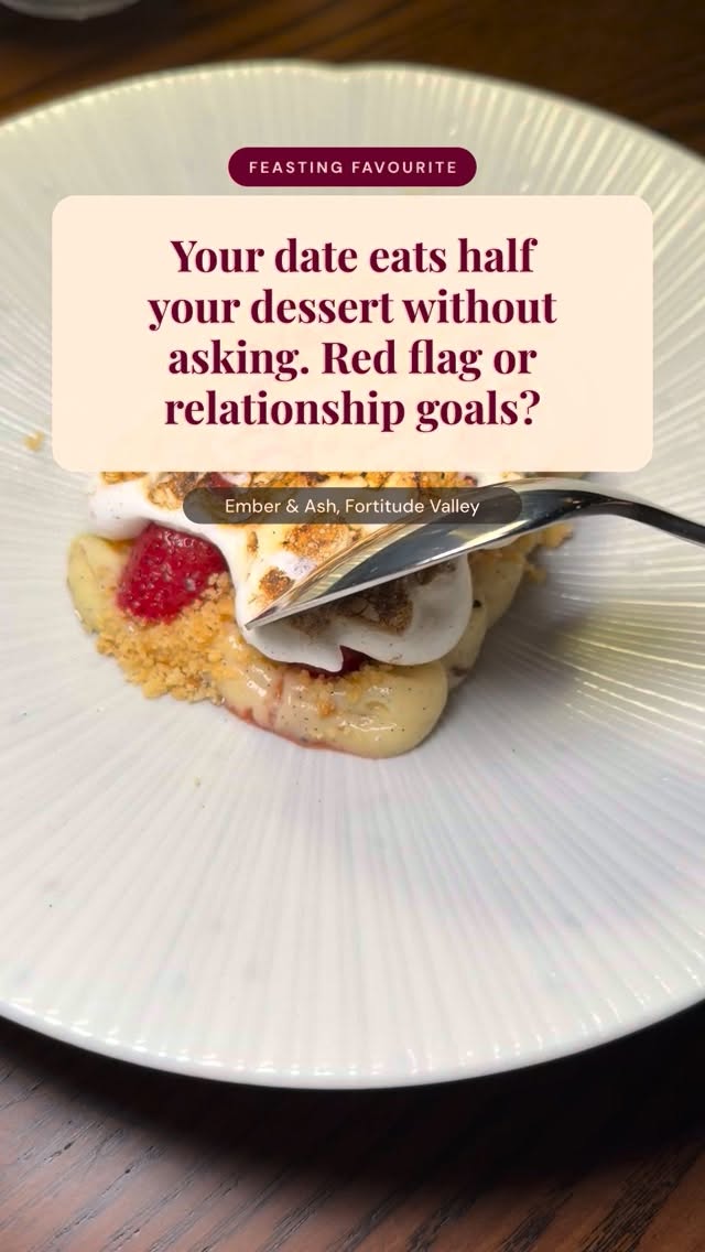 A white plate showcasing a dessert crafted with fresh raspberries, custard, golden crumble, and whipped meringue, with a metal spoon cutting in.