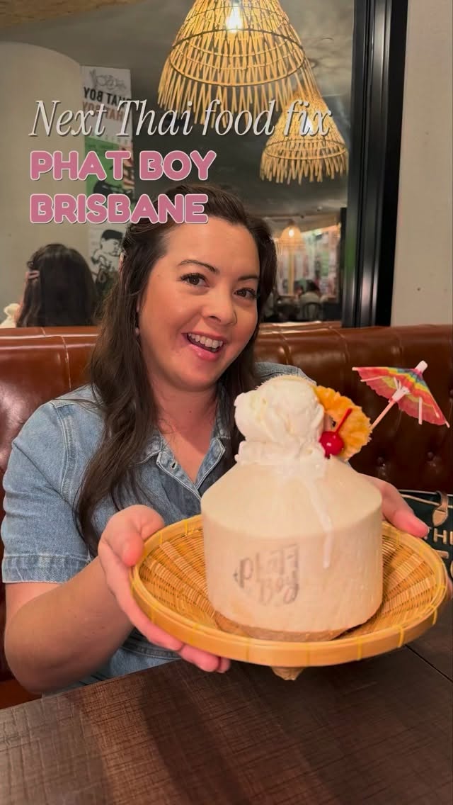 Zen holding a coconut dessert served inside a whole young coconut garnished with ice cream, pineapple, cherry, and a mini paper umbrella at Phat Boy.