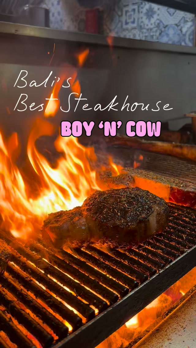 Thick steaks searing over bright open flames on a grill at Boy 'N' Cow steakhouse in Seminyak Bali.