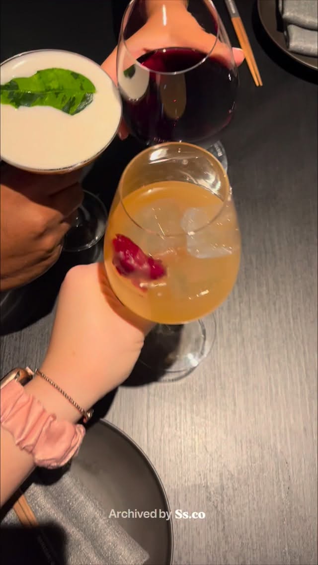 Three cocktail glasses held up in a toast over a dark wooden table at Mamasan Kitchen & Bar.